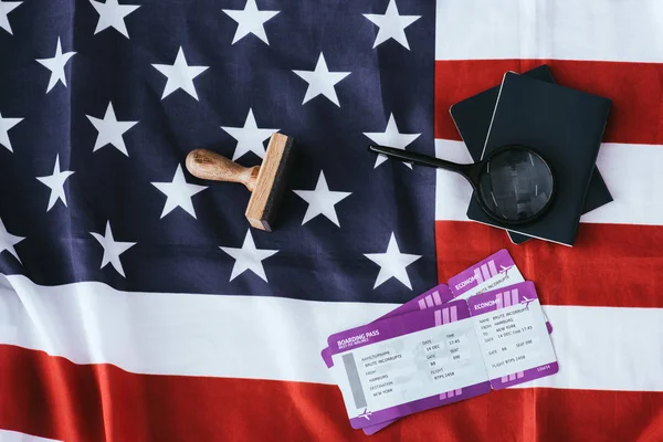 Vista superior de pasaportes y lupa cerca de boletos y bandera americana - foto de stock
