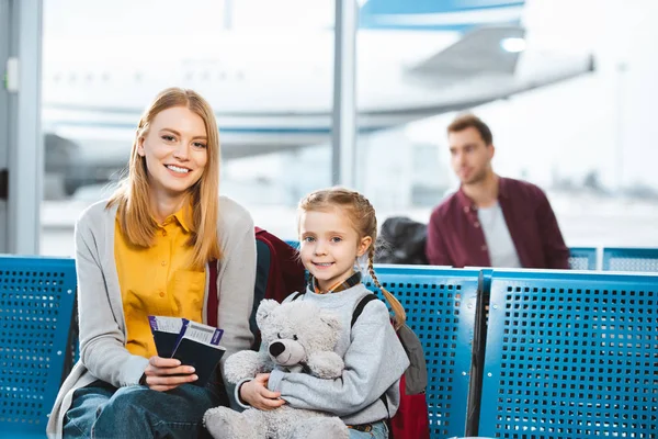 Selective focus of mother holding passports with air tickets and smiling near daughter in airport in departure lounge — Stock Photo
