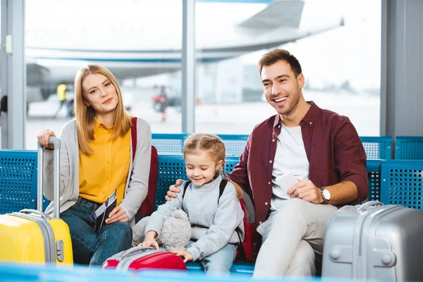 Familia feliz esperando en la sala de salida y sonriendo cerca de equipaje - foto de stock