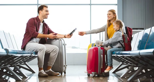 Sonriente padre dando pasaportes con billetes de avión a la esposa cerca de hija en el aeropuerto - foto de stock