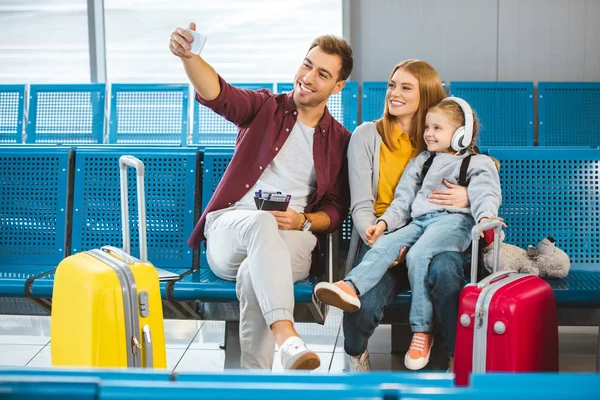 Familia alegre tomando selfie y sonriendo en el aeropuerto cerca de equipaje - foto de stock