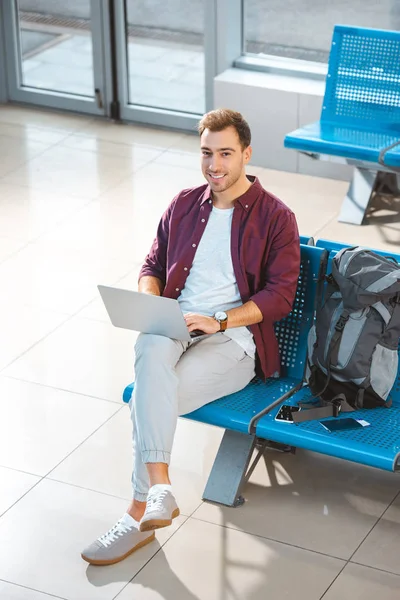 Visão aérea do homem sorridente usando laptop enquanto espera na sala de embarque — Fotografia de Stock