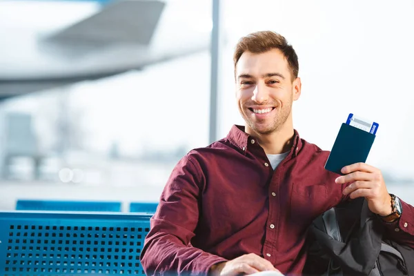 Hombre alegre con pasaporte con billete de avión en la sala de espera del aeropuerto - foto de stock