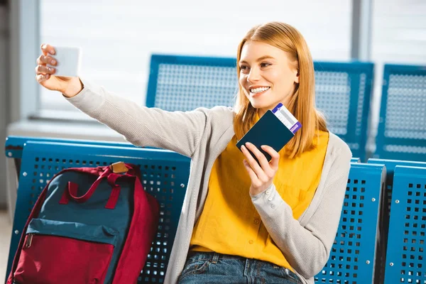 Усміхнена жінка бере селфі з паспортом та авіаквитком у залі очікування — стокове фото