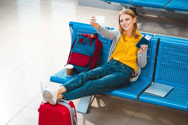Mujer sonriente tomando selfie en aeropuerto cerca de mochila y equipaje - foto de stock
