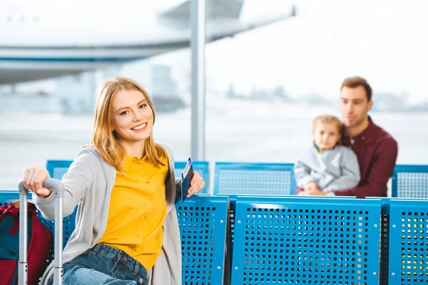 Enfoque selectivo de la mujer con pasaporte con billete de avión y sonriendo con la gente en el fondo - foto de stock