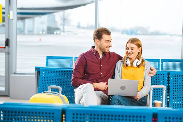 Hombre feliz mirando a la novia con portátil en el aeropuerto - foto de stock
