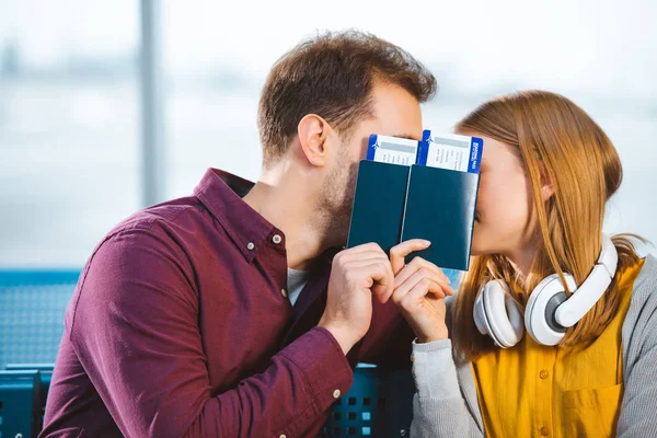 Novio y novia cubriendo caras con pasaportes en el aeropuerto - foto de stock