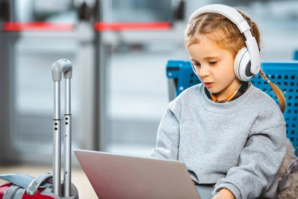 Lindo niño en los auriculares con ordenador portátil en el aeropuerto - foto de stock