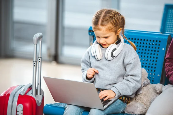 Cute child in headphones using laptop in airport — Stock Photo