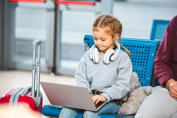 Cute kid in headphones using laptop near dad in waiting hall of airport — Stock Photo