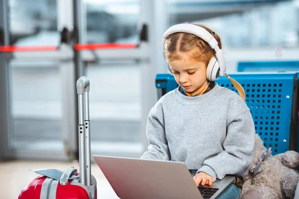 Adorable child listening music in headphones and using laptop in waiting hall — Stock Photo