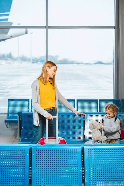Привабливі матері, стоячи з Симпатичні дочка холдингу плюшевого ведмедика поблизу багажу в аеропорту — стокове фото