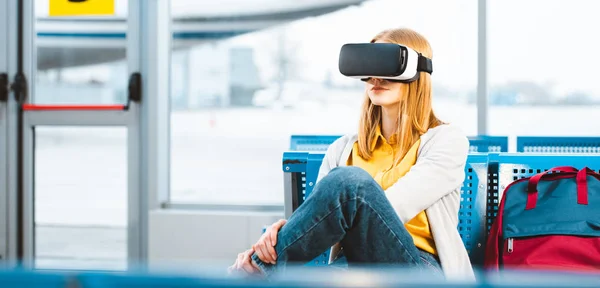 Mulher vestindo fone de ouvido realidade virtual enquanto espera na sala de partida perto da mochila — Fotografia de Stock