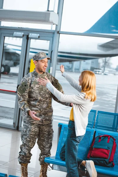 Happy woman looking at boyfriend in military uniform and standing with opened arms — Stock Photo