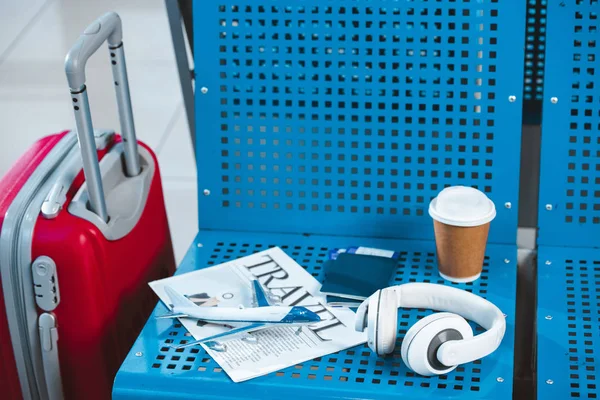Модель самолета на туристической газете возле бумажной чашки и чемодана в аэропорту — стоковое фото