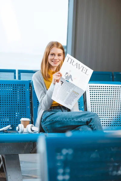 Attraktive Frau lächelt, während sie die Reisezeitung in der Abflughalle hält — Stockfoto