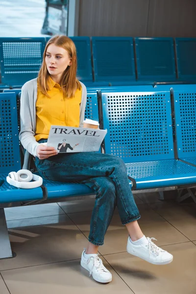 Atractiva mujer leyendo periódico cerca de auriculares en el aeropuerto - foto de stock