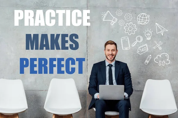 Smiling businessman sitting on chair and using laptop in waiting hall with practice makes perfect lettering on wall — Stock Photo