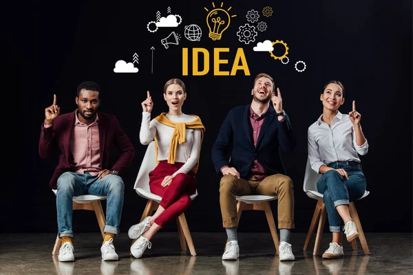 Multiethnic group of people sitting on chairs and showing idea gestures with idea illustration above heads isolated on black — Stock Photo