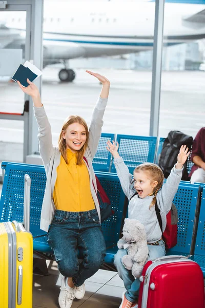 Querida madre e hija cogidas de la mano por encima de la cabeza y sonriendo en el aeropuerto - foto de stock