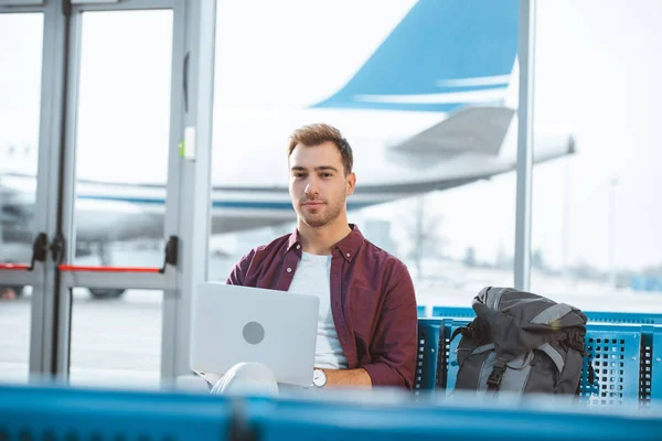 Schöner Mann benutzt Laptop, während er in der Abflughalle wartet — Stockfoto