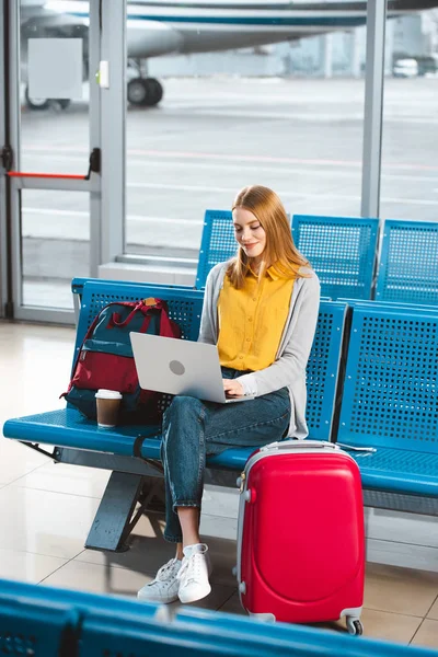 Hermosa mujer sentada con el ordenador portátil cerca de la mochila y el equipaje en la sala de espera - foto de stock