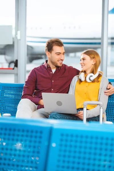 Lächelndes Paar schaut sich am Flughafen in der Nähe des Laptops an — Stockfoto