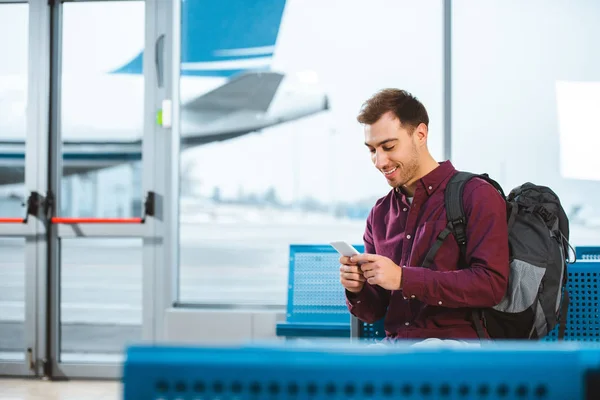 Cheerful man using smartphone and smiling while waiting in departure lounge — Stock Photo
