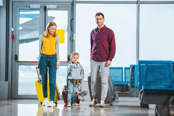 Cute kid holding teddy bear and standing with mom and dad in waiting hall — Stock Photo