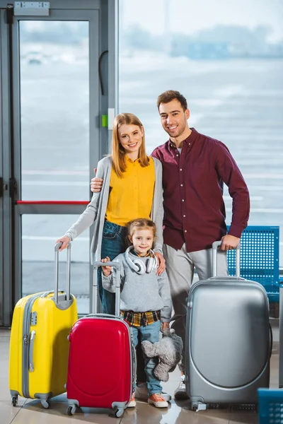 Felice famiglia in piedi con bagagli nella sala partenze — Foto stock