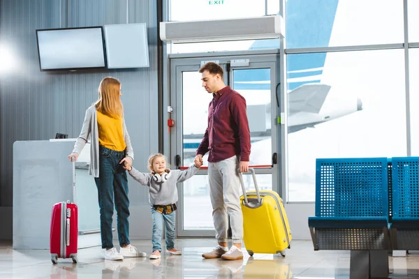 Esposa y marido tomados de la mano con la hija y de pie maletas limpias en el aeropuerto - foto de stock