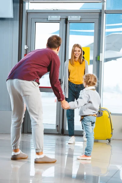 Веселая мать смотрит на дочь и мужа, держащихся за руки в аэропорту — стоковое фото