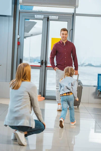 Hija corriendo a papá alegre mientras se reúnen en el aeropuerto - foto de stock