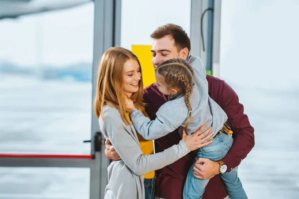 Familia alegre sonriendo mientras se abraza en el aeropuerto - foto de stock