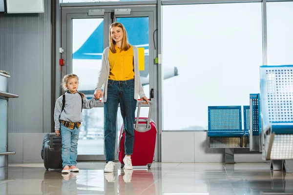 Joyeuse mère tenant la main avec fille mignonne à l'aéroport — Photo de stock