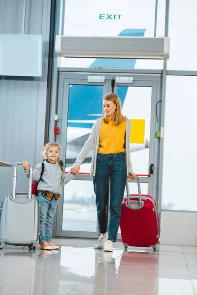Весела мати дивиться на дочку, тримаючись за руки в аеропорту — стокове фото