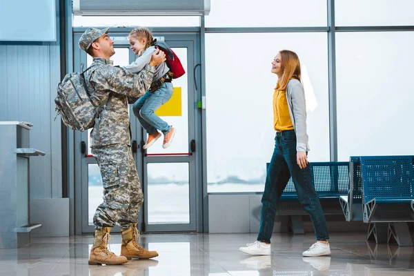 Happy father in military uniform holding in arms cute daughter near wife in airport — Stock Photo