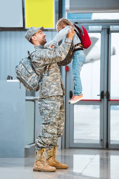 Glücklicher Vater in Militäruniform, der seine süße Tochter im Flughafen in den Armen hält — Stockfoto