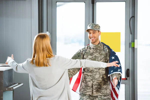 Вибірковий фокус щасливого хлопця у військовій формі, дивлячись на подругу з відкритими руками в аеропорту — стокове фото