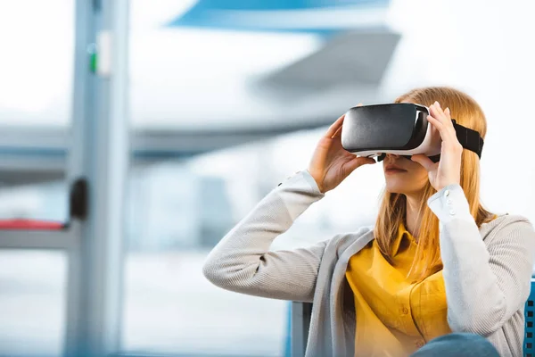 Femme portant un casque de réalité virtuelle assis dans le salon de départ — Photo de stock