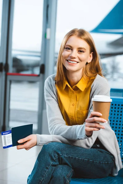 Atractiva mujer sonriendo mientras sostiene la taza desechable en el aeropuerto - foto de stock