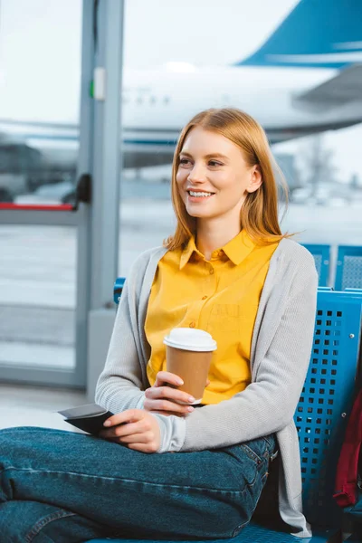 Mulher atraente segurando copo descartável enquanto sentado no aeroporto — Fotografia de Stock