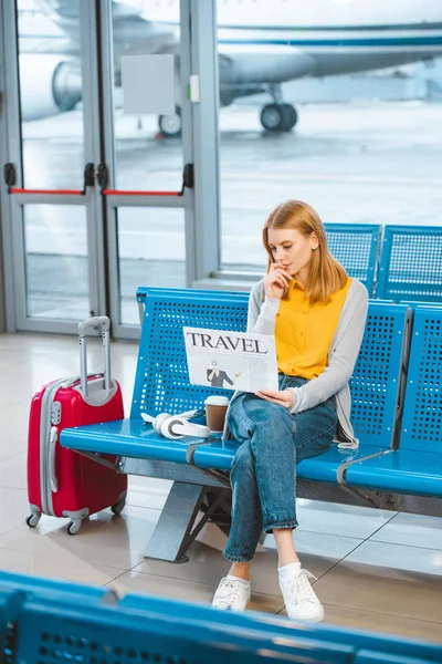 Привлекательная женщина читает туристическую газету возле чемодана в аэропорту — стоковое фото