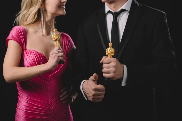 KYIV, UCRANIA - 10 DE ENERO DE 2019: vista parcial del hombre mostrando el pulgar hacia arriba y sosteniendo premios Oscar con la mujer aislada en negro - foto de stock