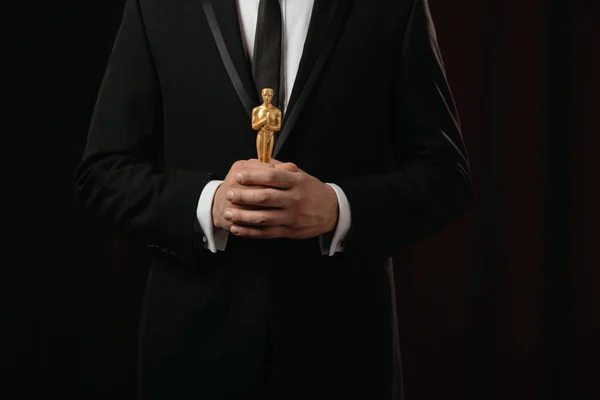 KYIV, UKRAINE - JANUARY 10, 2019: cropped view of man in suit holding oscar award on dark background — Stock Photo