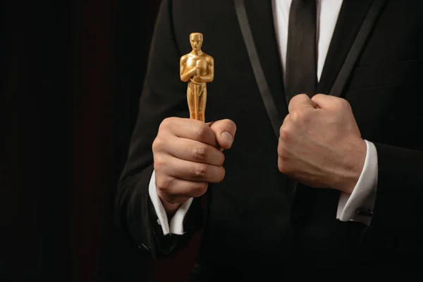 КИЕВ, УКРАИНА - 10 ЯНВАРЯ 2019 года: частичный взгляд человека в костюме с сжатым кулаком, держащим Оскар в руках, изолированный на черном — стоковое фото