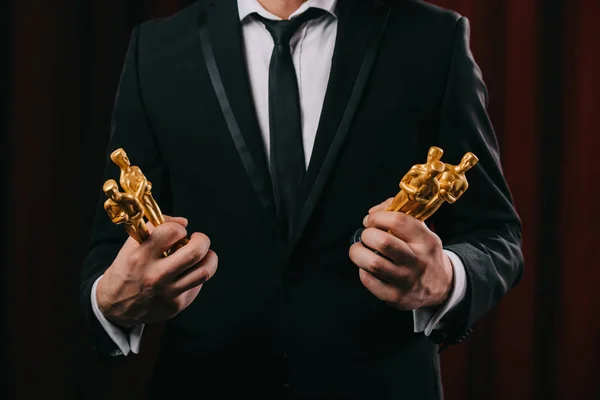 KYIV, UKRAINE - JANUARY 10, 2019: partial view of man in suit holding oscar awards on dark background — Stock Photo