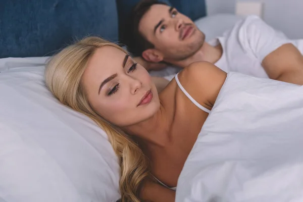 Ревнивая молодая пара, лежащая вместе в постели и глядя в сторону, концепция проблемы отношений — стоковое фото