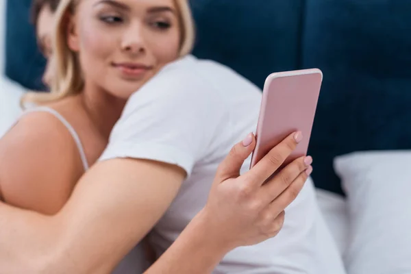 Selective focus of young woman using smartphone and lying with boyfriend in bed — Stock Photo